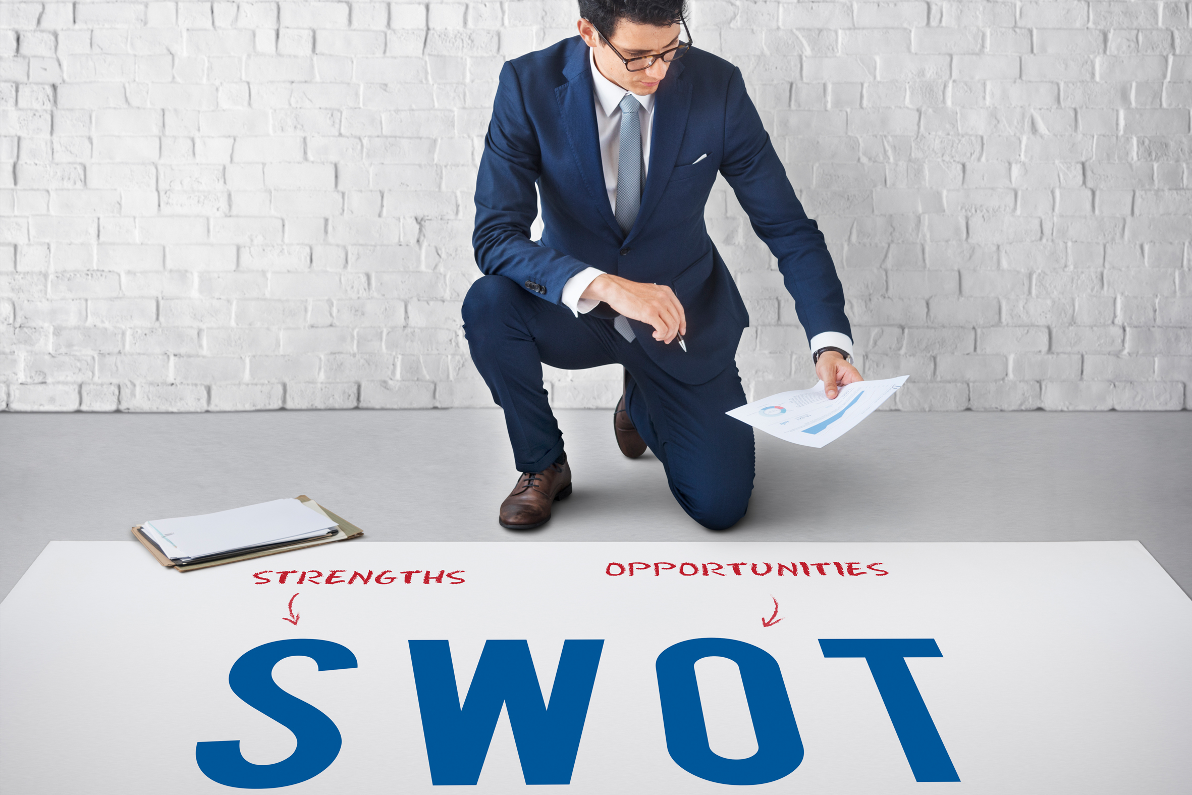 Cheerful young businessman with report in hand talking to female colleague who is making copies of documents